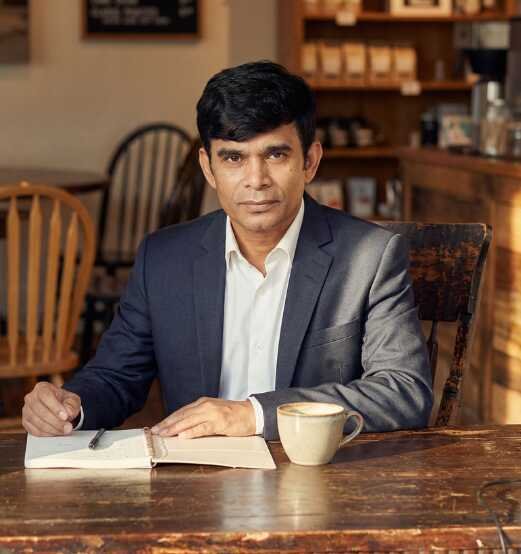 Magician Sooraj, professional mentalist, seated at a wooden table with a notebook and coffee in a warm, elegant café setting.